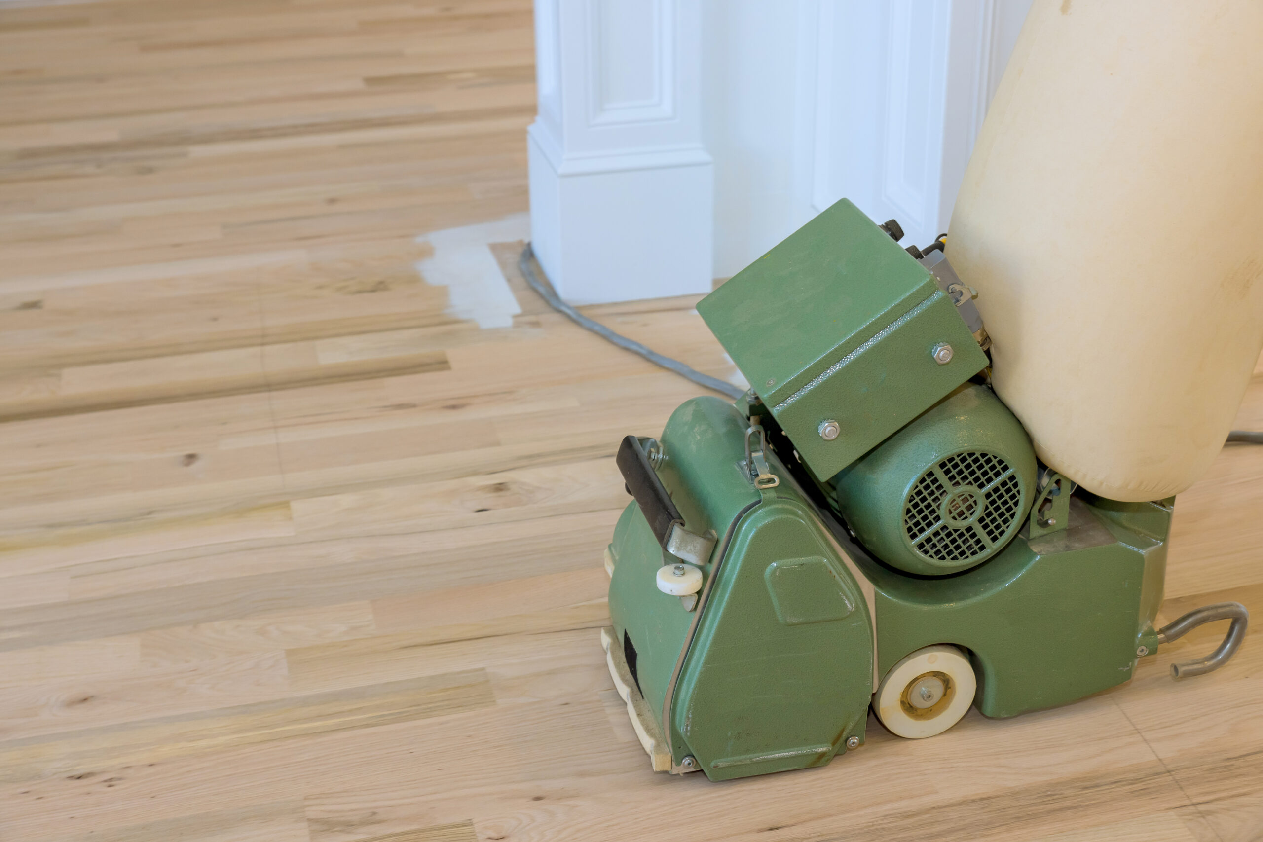 Using a floor sander carpenter grinds wood parquet floors in new house that has just been built